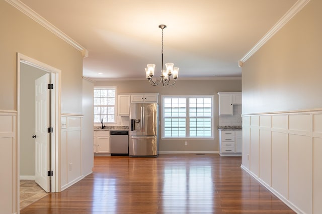 kitchen featuring white cabinets, appliances with stainless steel finishes, backsplash, a chandelier, and crown molding