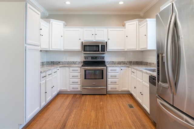 kitchen with stainless steel appliances, backsplash, white cabinetry, and light stone counters