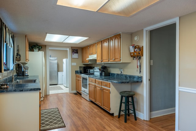 kitchen with sink, electric range, light wood-type flooring, a textured ceiling, and a kitchen bar