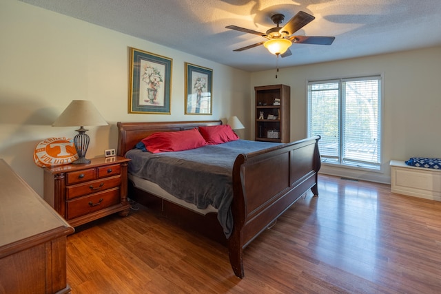 bedroom with ceiling fan, wood-type flooring, and a textured ceiling