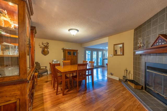 dining area with hardwood / wood-style floors, a tile fireplace, french doors, tile walls, and a textured ceiling