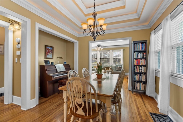 dining room with ornamental molding, light wood-type flooring, and a tray ceiling