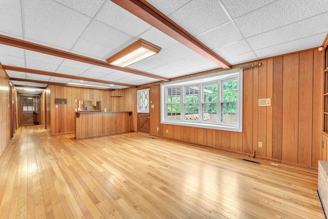 unfurnished living room with light wood-type flooring, a drop ceiling, and wooden walls