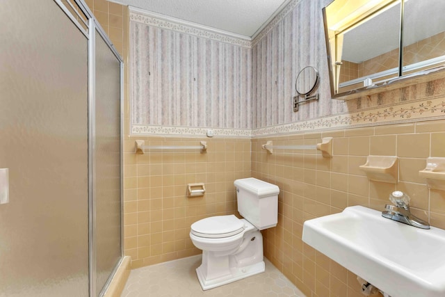 full bathroom with a stall shower, a wainscoted wall, wallpapered walls, and a sink