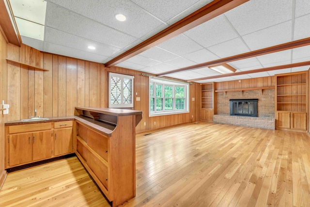 interior space featuring a drop ceiling, light wood-style floors, wood walls, and a fireplace