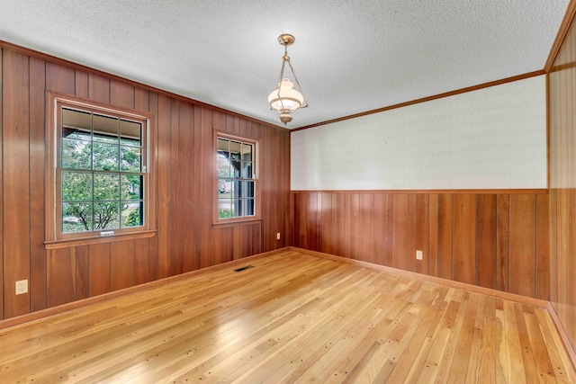 empty room featuring a textured ceiling, ornamental molding, visible vents, wooden walls, and hardwood / wood-style floors