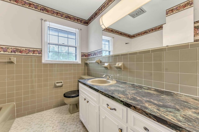 full bath featuring toilet, tile walls, vanity, visible vents, and wainscoting
