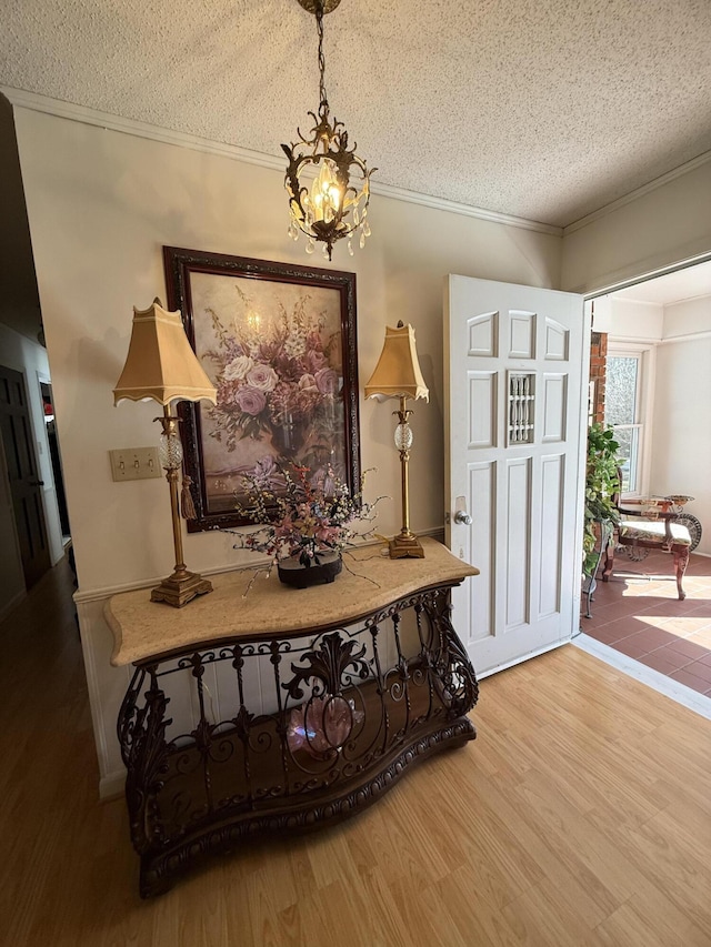 entrance foyer featuring a textured ceiling, an inviting chandelier, wood finished floors, and crown molding