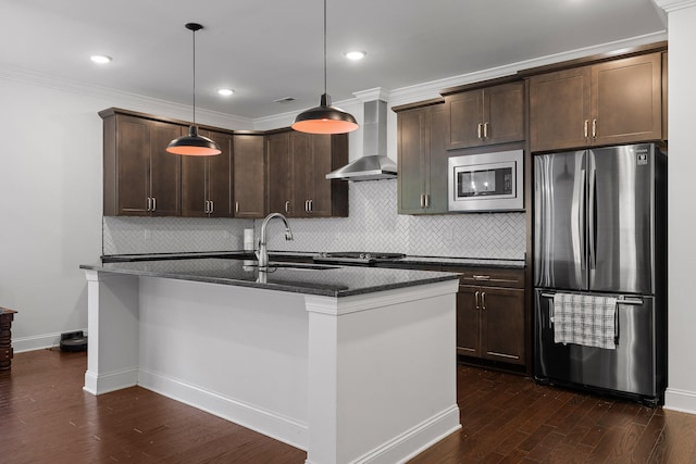 kitchen with dark wood-type flooring, stainless steel appliances, wall chimney range hood, an island with sink, and pendant lighting