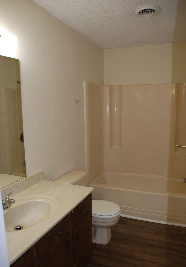 full bathroom featuring wood-type flooring, a textured ceiling, toilet, and  shower combination