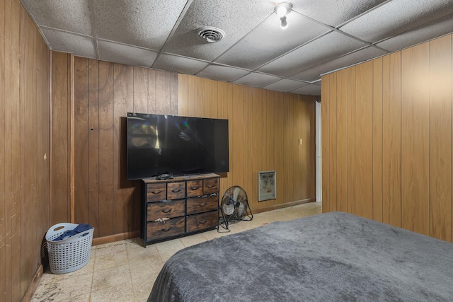 bedroom featuring baseboards, wood walls, visible vents, and a paneled ceiling