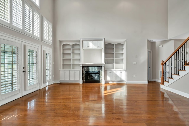 unfurnished living room with stairs, baseboards, wood finished floors, and a towering ceiling