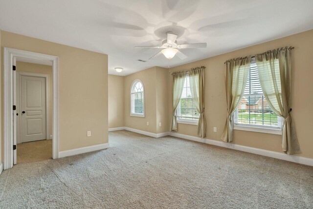 carpeted empty room with visible vents, a ceiling fan, and baseboards