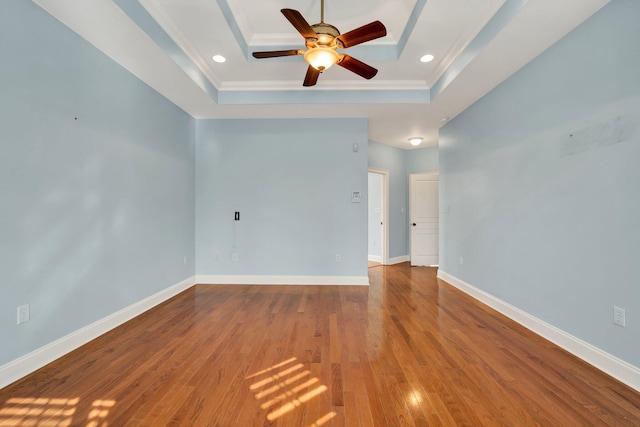 unfurnished room featuring a raised ceiling, wood finished floors, recessed lighting, baseboards, and ceiling fan