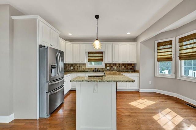 kitchen featuring wood finished floors, visible vents, stainless steel fridge, white cabinets, and tasteful backsplash