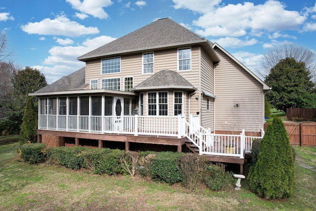 rear view of house with fence, a sunroom, a shingled roof, a deck, and a lawn