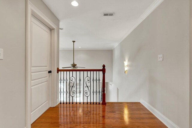 hallway featuring wood finished floors, an upstairs landing, visible vents, and ornamental molding