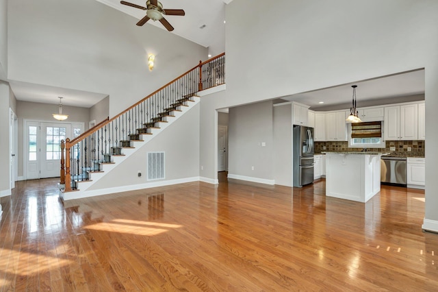 unfurnished living room featuring visible vents, light wood-style flooring, stairs, and baseboards