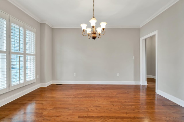 empty room featuring an inviting chandelier, wood finished floors, baseboards, and ornamental molding