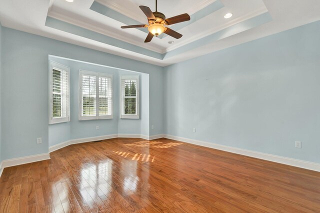 unfurnished room with crown molding, baseboards, hardwood / wood-style flooring, a raised ceiling, and a ceiling fan