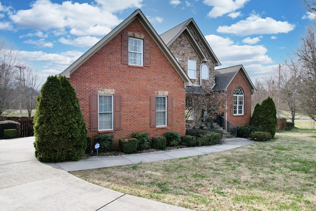 view of side of property with stone siding, a yard, roof with shingles, concrete driveway, and brick siding