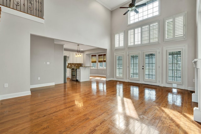 unfurnished living room featuring crown molding, ceiling fan with notable chandelier, baseboards, and wood-type flooring