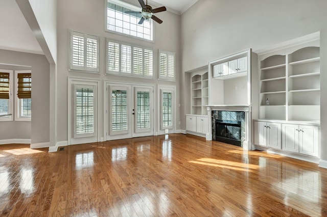 unfurnished living room featuring a wealth of natural light, light wood finished floors, baseboards, and a high end fireplace