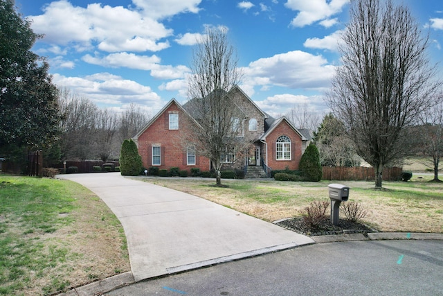 traditional home featuring brick siding, a front lawn, and fence