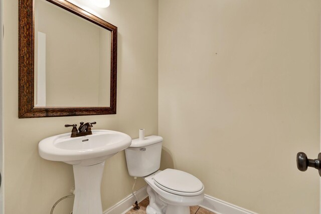 half bathroom featuring a sink, baseboards, toilet, and tile patterned flooring