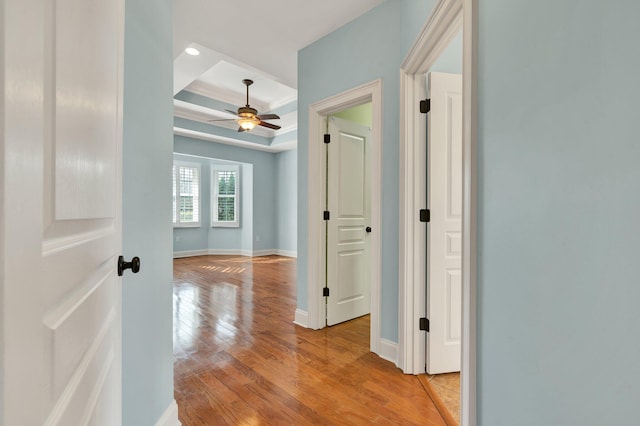 hallway with a tray ceiling, baseboards, and light wood finished floors