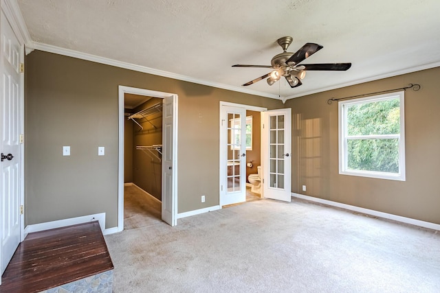 unfurnished bedroom featuring a closet, a spacious closet, ornamental molding, and french doors