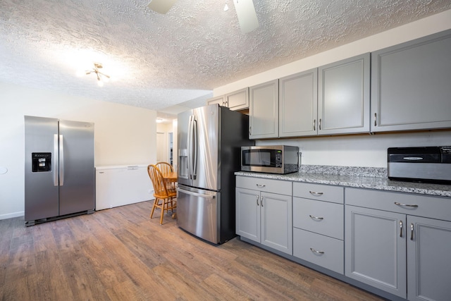 kitchen with light stone countertops, appliances with stainless steel finishes, ceiling fan, dark wood-type flooring, and gray cabinets