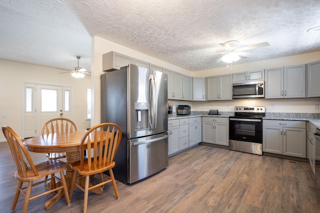 kitchen with gray cabinets, light stone counters, dark hardwood / wood-style flooring, and stainless steel appliances