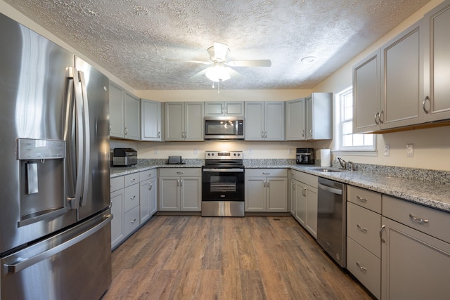 kitchen featuring gray cabinetry, ceiling fan, light stone countertops, dark hardwood / wood-style flooring, and stainless steel appliances