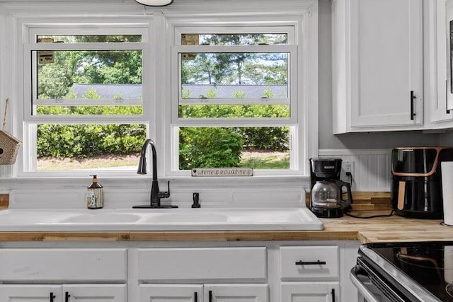 interior space with electric range, sink, and white cabinets