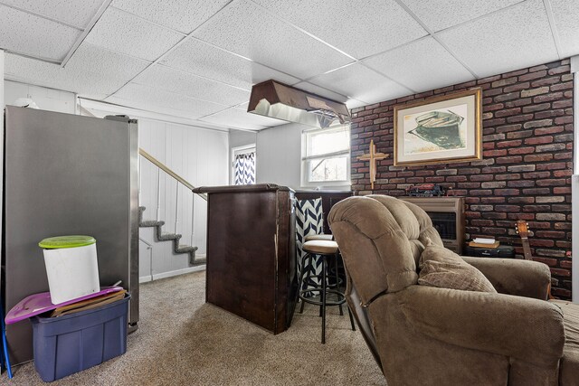 carpeted living room featuring a paneled ceiling and brick wall