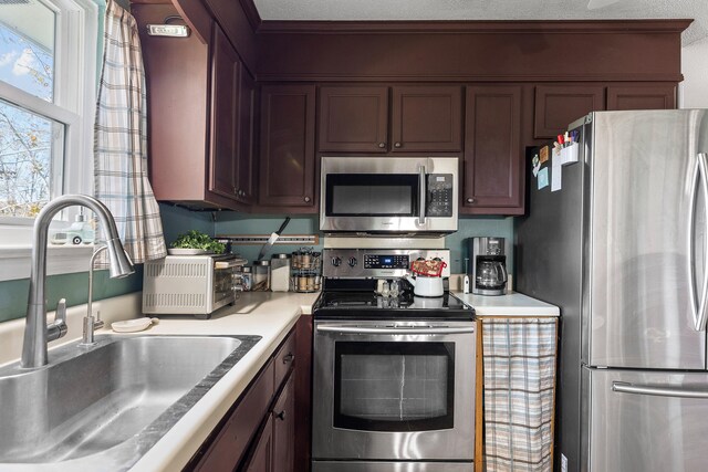 kitchen featuring appliances with stainless steel finishes, ornamental molding, dark brown cabinets, a textured ceiling, and sink