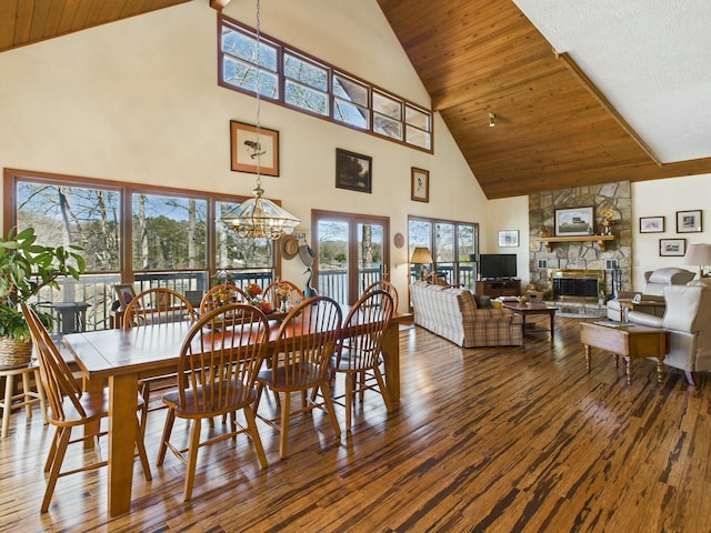 dining space featuring wood ceiling, a stone fireplace, hardwood / wood-style flooring, and an inviting chandelier