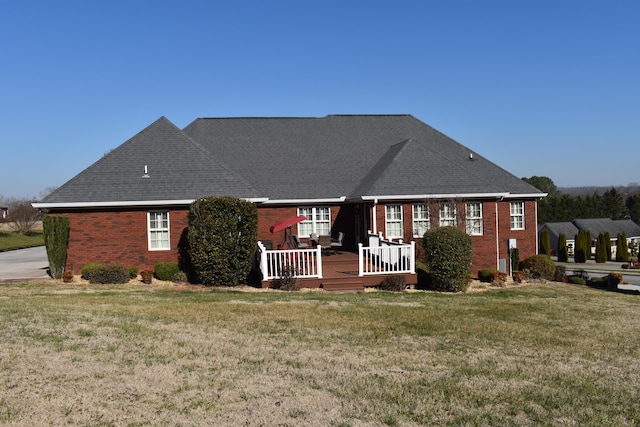 view of front of home featuring brick siding, roof with shingles, a deck, and a front yard