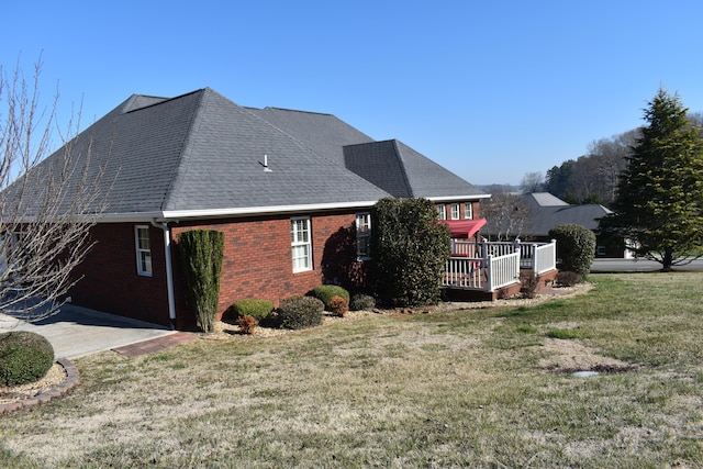 view of side of property with brick siding, a wooden deck, a yard, and roof with shingles