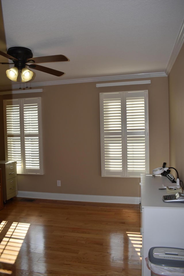 interior space with baseboards, a ceiling fan, wood finished floors, and crown molding