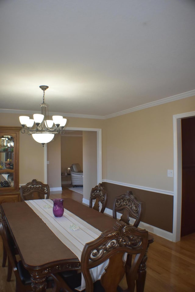 dining area with a notable chandelier, ornamental molding, and wood finished floors