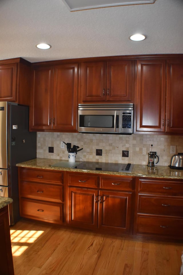 kitchen with light wood-style flooring, light stone counters, tasteful backsplash, and appliances with stainless steel finishes