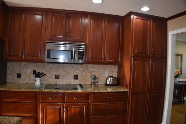 kitchen featuring light stone counters, stainless steel microwave, black electric stovetop, and decorative backsplash