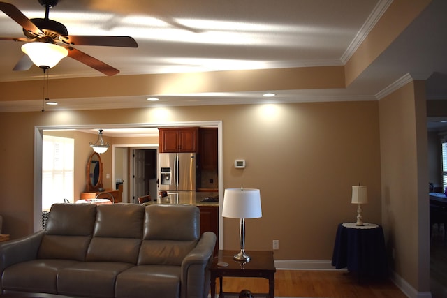 living room with a raised ceiling, wood finished floors, recessed lighting, crown molding, and baseboards