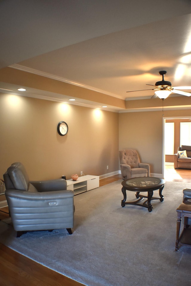 living area with a tray ceiling, baseboards, carpet, and crown molding