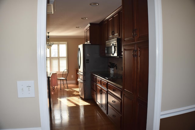 kitchen featuring black electric stovetop, dark wood-type flooring, stainless steel microwave, crown molding, and baseboards