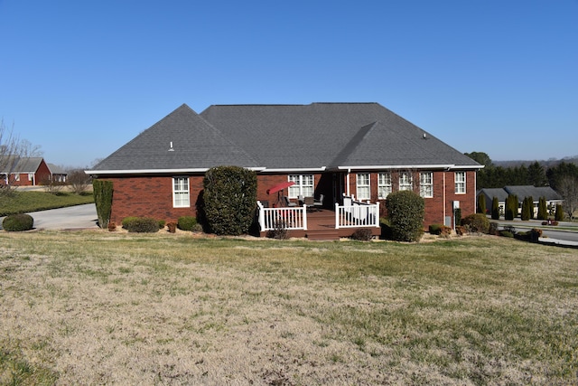 back of property with brick siding, a deck, a yard, and roof with shingles