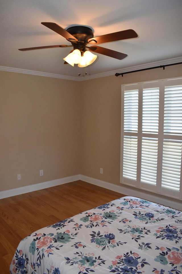 unfurnished bedroom featuring ceiling fan, wood finished floors, baseboards, and ornamental molding