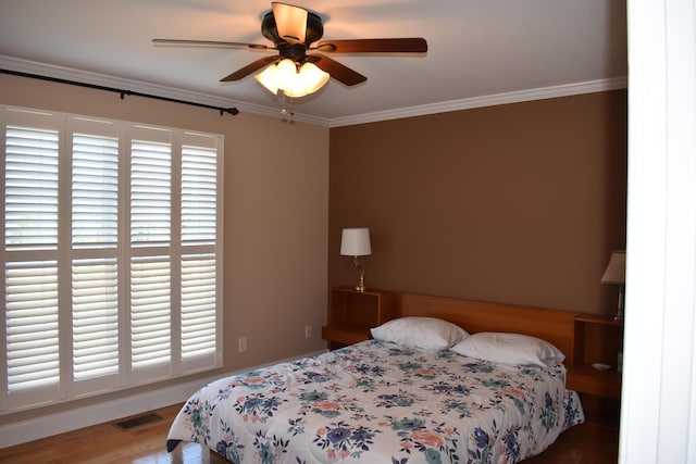 bedroom with a ceiling fan, wood finished floors, visible vents, and ornamental molding